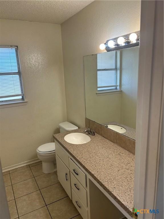 bathroom with vanity, a healthy amount of sunlight, tile patterned flooring, a textured ceiling, and toilet