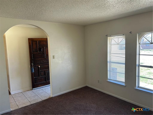 unfurnished room with light carpet, a textured ceiling, arched walkways, light tile patterned floors, and baseboards