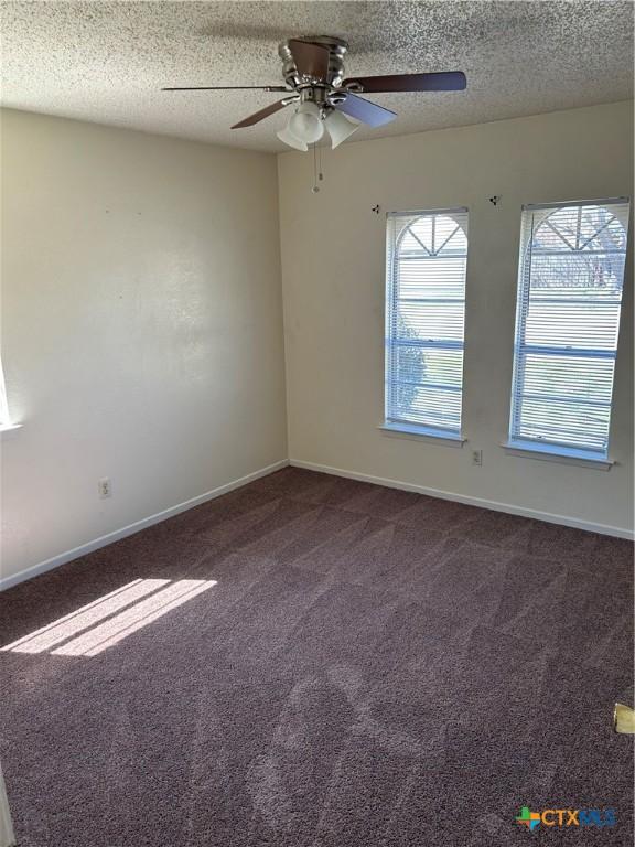 empty room featuring dark carpet, a textured ceiling, baseboards, and a ceiling fan