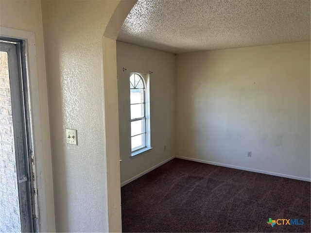 spare room featuring a textured ceiling, dark carpet, arched walkways, baseboards, and a textured wall