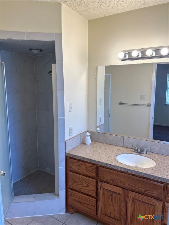 bathroom featuring tile patterned floors, a textured ceiling, vanity, and a tile shower