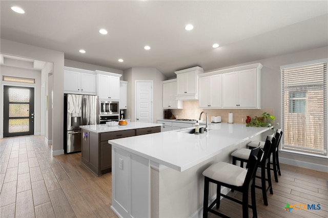 kitchen with white cabinetry, sink, stainless steel appliances, kitchen peninsula, and a breakfast bar area