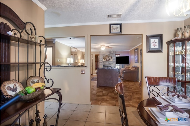 tiled dining room featuring a fireplace, a textured ceiling, ceiling fan, and crown molding