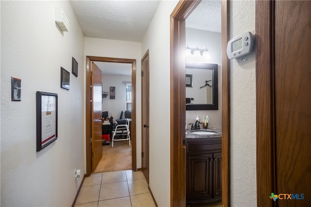 hall featuring sink, light tile patterned floors, and a textured ceiling