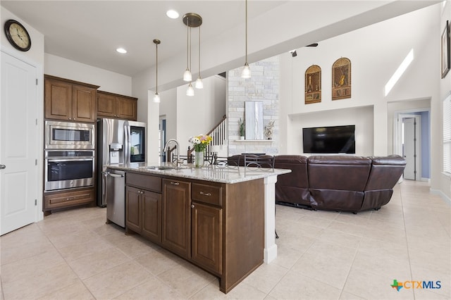 kitchen featuring stainless steel appliances, a sink, a center island with sink, light stone countertops, and light tile patterned floors