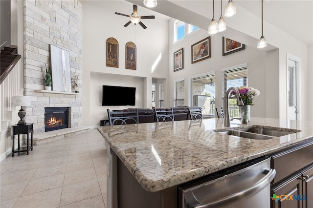 kitchen with a stone fireplace, a ceiling fan, stainless steel dishwasher, a sink, and open floor plan