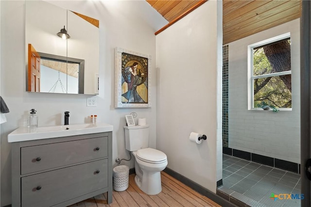 bathroom featuring toilet, wood finished floors, vanity, baseboards, and tiled shower