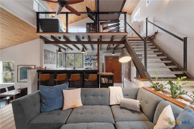 living room featuring high vaulted ceiling, beam ceiling, stairway, and wood finished floors