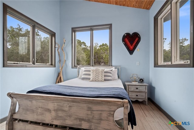 bedroom with lofted ceiling, multiple windows, baseboards, and wood finished floors