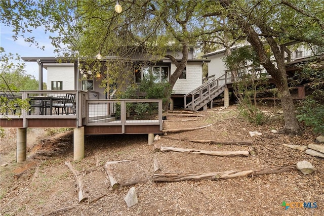 rear view of house featuring brick siding, stairway, and a wooden deck