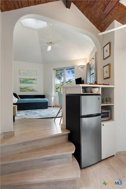 kitchen with ceiling fan, arched walkways, light wood-style floors, vaulted ceiling, and freestanding refrigerator