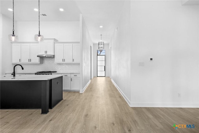 kitchen with under cabinet range hood, light wood-style floors, white cabinets, light countertops, and backsplash