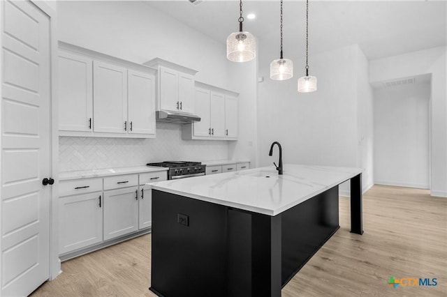 kitchen featuring under cabinet range hood, a sink, white cabinetry, light wood finished floors, and decorative light fixtures