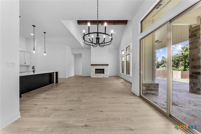 unfurnished living room with baseboards, a fireplace with raised hearth, a towering ceiling, light wood-style flooring, and beamed ceiling