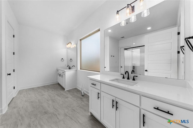 bathroom with recessed lighting, two vanities, an enclosed shower, a sink, and baseboards