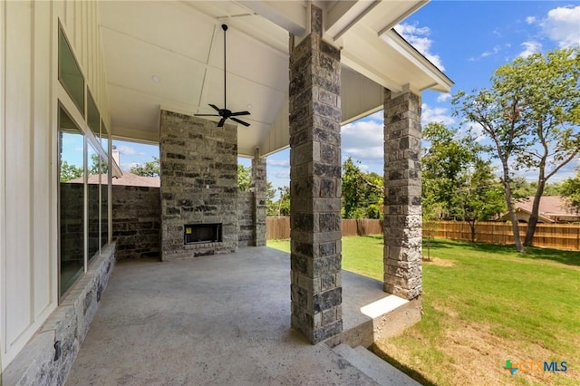 view of patio featuring ceiling fan, an outdoor stone fireplace, and fence