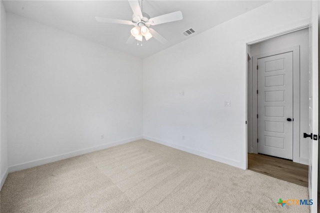 carpeted spare room featuring ceiling fan, visible vents, and baseboards