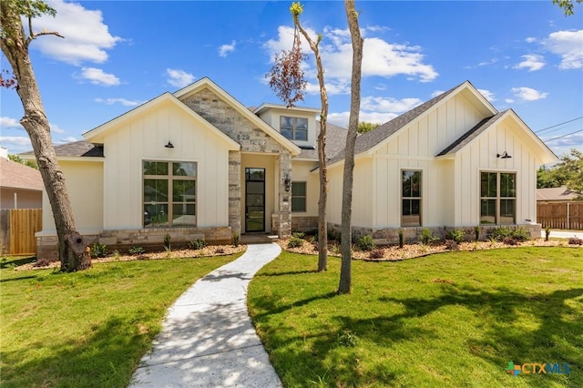 modern inspired farmhouse featuring fence, stone siding, roof with shingles, a front lawn, and board and batten siding