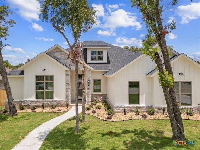 modern farmhouse style home with stone siding, a front lawn, board and batten siding, and roof with shingles