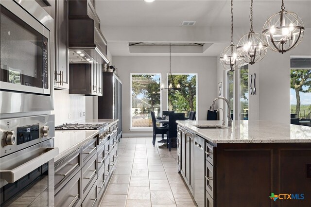 kitchen with dark brown cabinets, a wealth of natural light, appliances with stainless steel finishes, and an island with sink