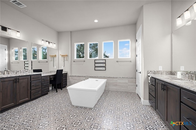 bathroom featuring a wealth of natural light, vanity, and tiled tub