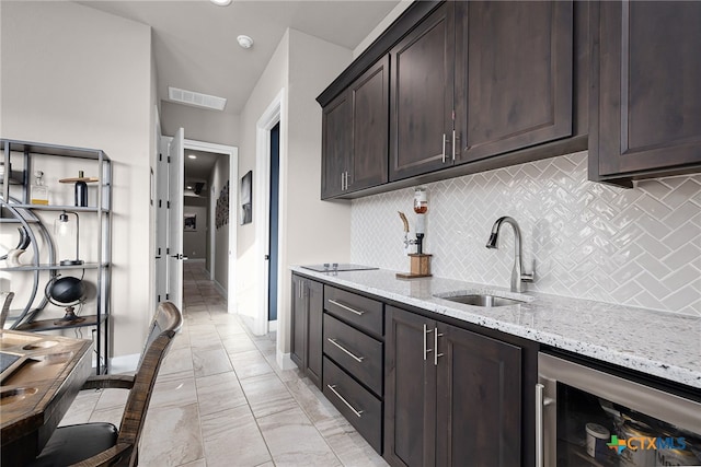 kitchen featuring decorative backsplash, sink, light stone countertops, dark brown cabinets, and wine cooler