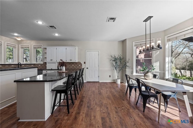 kitchen featuring dark wood-type flooring, white cabinetry, a kitchen breakfast bar, backsplash, and dark countertops