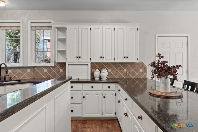 kitchen with tasteful backsplash, dark stone countertops, dark wood-type flooring, white cabinetry, and a sink