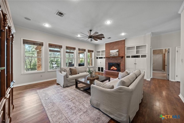 living room with a brick fireplace, visible vents, dark wood-type flooring, and ornamental molding