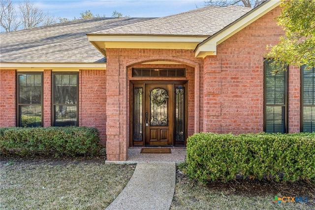 view of exterior entry featuring a shingled roof and brick siding