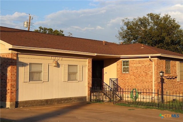 rear view of property with roof with shingles, brick siding, and fence