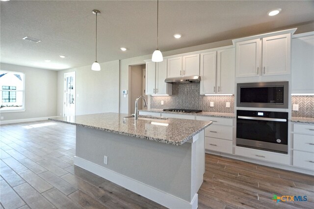 kitchen with dark wood-type flooring, under cabinet range hood, a sink, tasteful backsplash, and stainless steel appliances