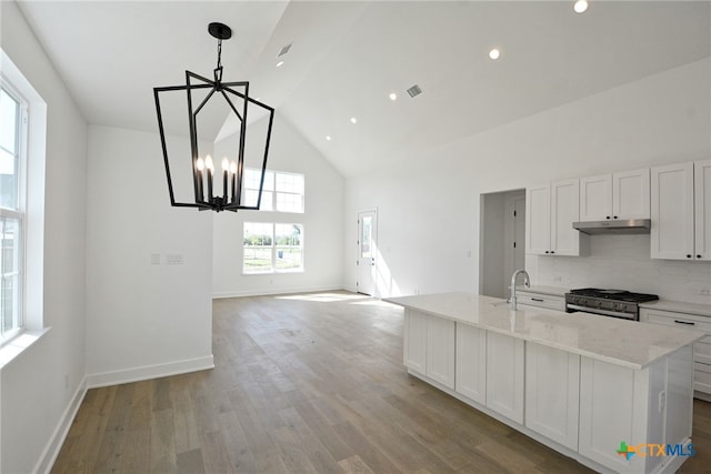 kitchen with white cabinetry, a center island with sink, tasteful backsplash, and stainless steel range with gas stovetop