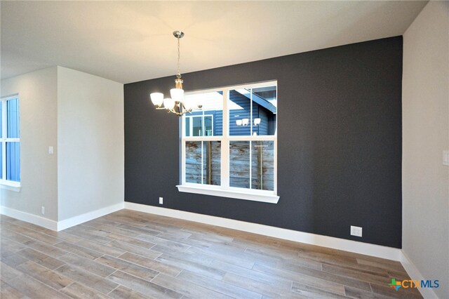 spare room with baseboards, an inviting chandelier, and wood finished floors