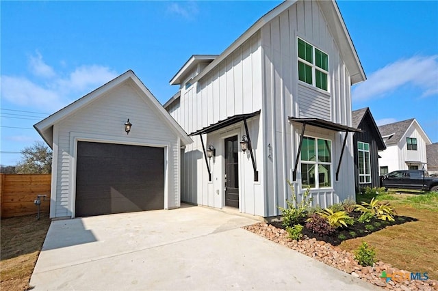 view of front facade with board and batten siding, fence, concrete driveway, a garage, and an outbuilding