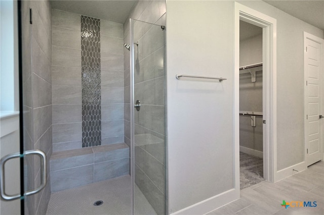 full bath featuring a shower stall, a walk in closet, and baseboards