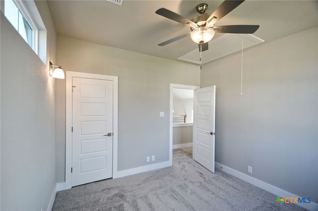 unfurnished bedroom featuring carpet flooring, attic access, baseboards, and a ceiling fan