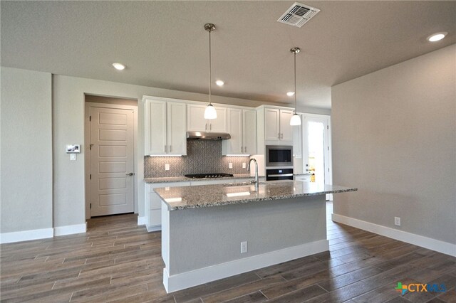 kitchen featuring visible vents, under cabinet range hood, dark wood finished floors, stainless steel appliances, and decorative backsplash