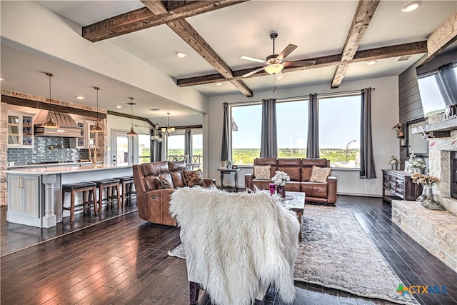 living room featuring beamed ceiling, a stone fireplace, ceiling fan with notable chandelier, and dark hardwood / wood-style flooring