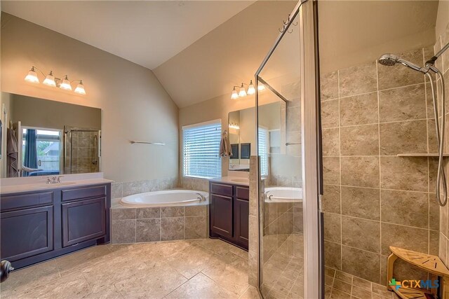 bathroom with a stall shower, lofted ceiling, a bath, and two vanities