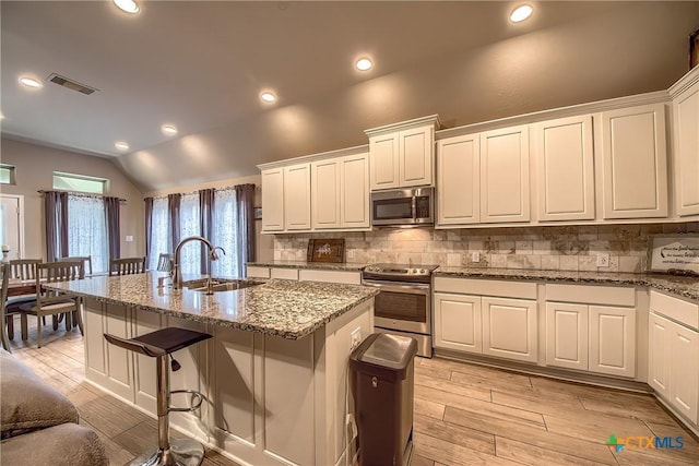 kitchen with tasteful backsplash, a sink, lofted ceiling, stainless steel appliances, and an island with sink