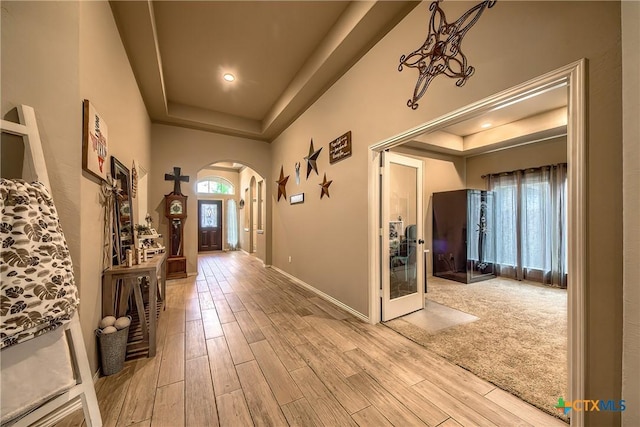 entryway with arched walkways, baseboards, wood finished floors, and a raised ceiling