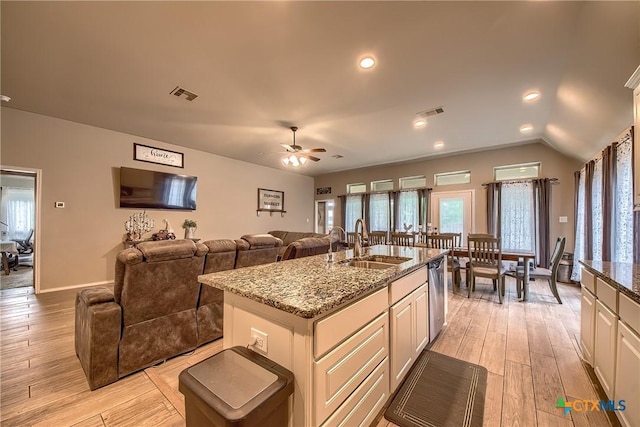 kitchen with a sink, light stone counters, light wood-style flooring, and visible vents