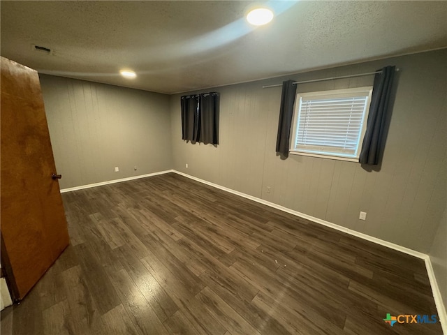 unfurnished room featuring dark wood-type flooring, a textured ceiling, and wooden walls