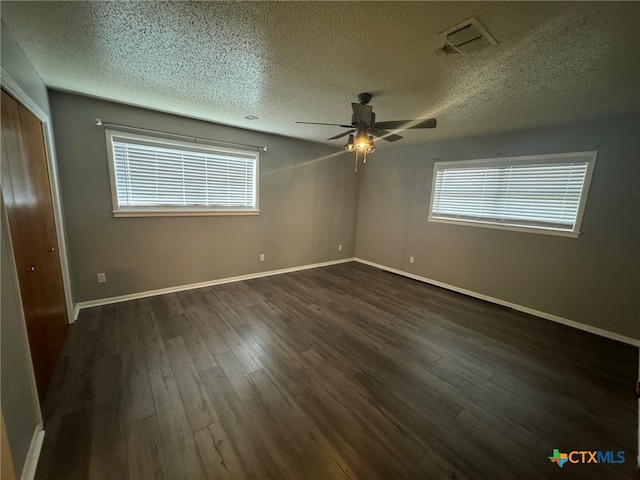 empty room featuring dark wood-type flooring, a healthy amount of sunlight, and a textured ceiling