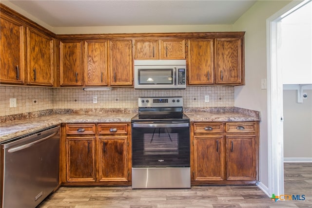 kitchen featuring decorative backsplash, light hardwood / wood-style flooring, stainless steel appliances, and light stone counters