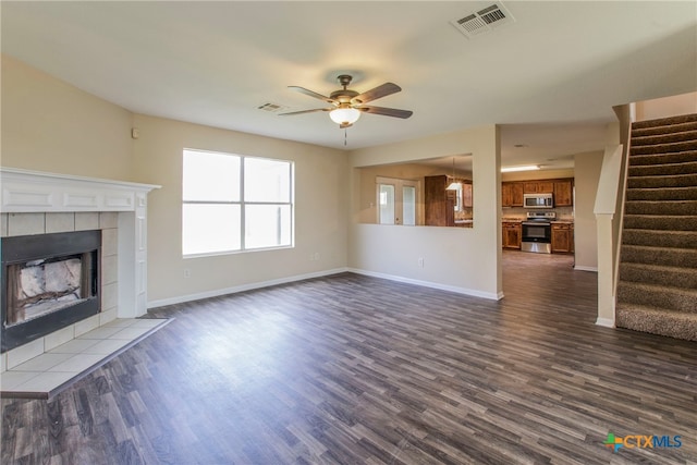 unfurnished living room with ceiling fan, dark wood-type flooring, and a tile fireplace