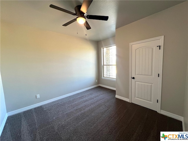 spare room featuring dark colored carpet and ceiling fan