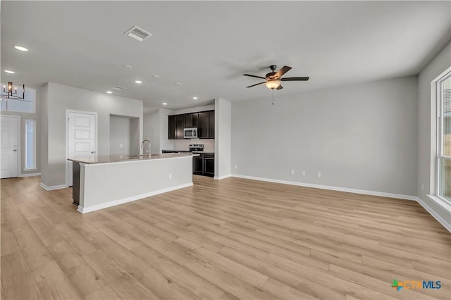 kitchen featuring a center island with sink, ceiling fan with notable chandelier, sink, light hardwood / wood-style flooring, and light stone countertops