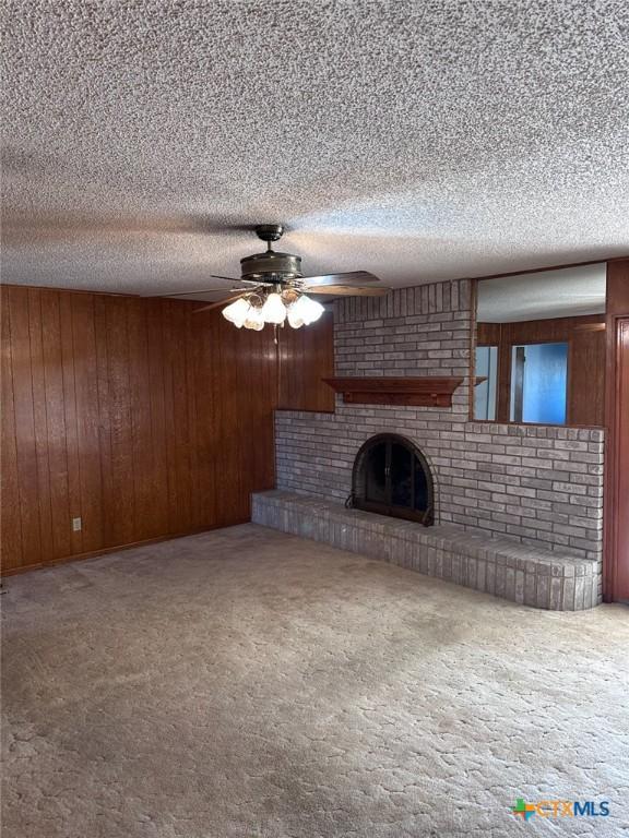 unfurnished living room with a brick fireplace, carpet flooring, and wooden walls